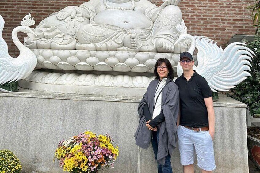 A couple standing in front of a large stone sculpture with swans and a lotus pond. 2