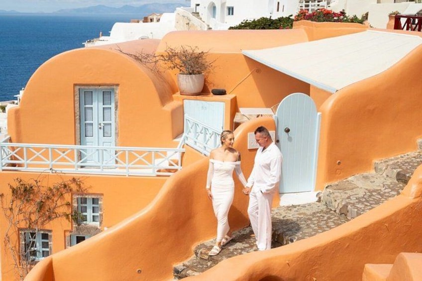 Un couple se tient devant un bâtiment orange aux lignes courbes, doté de portes et de balustrades blanches, et d’où l’on a une vue sur la mer. 5