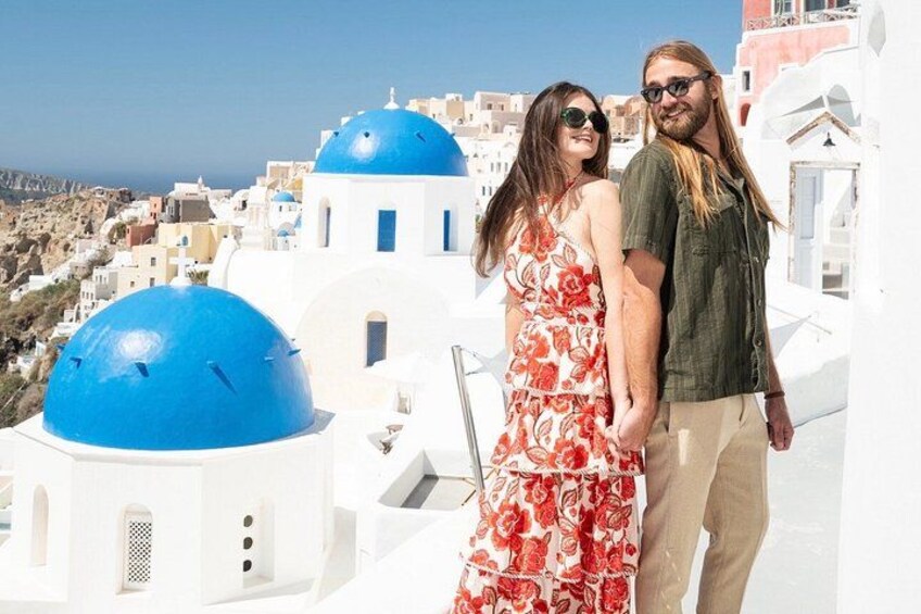 Un couple se tient sur un toit, avec en arrière-plan des bâtiments blancs et des dômes bleus. 2