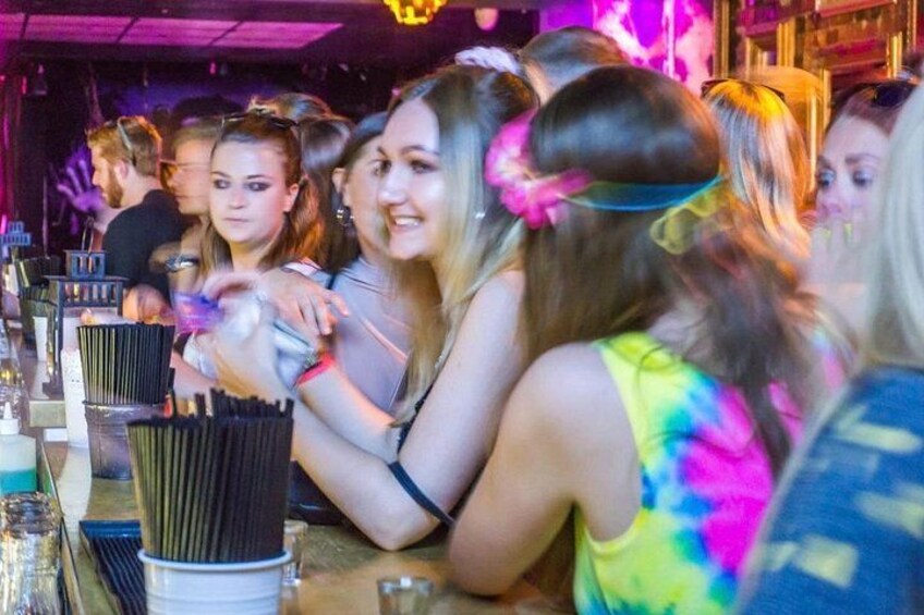 A group of people at a bar with drinks and glasses on the counter. 2