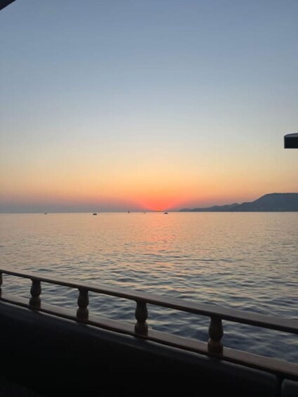 A sunset over a calm sea with a railing in the foreground. 1