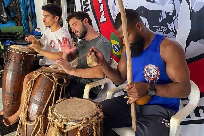 Three individuals seated, playing drums. 4