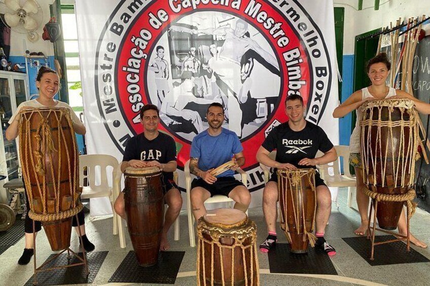 Four people seated on chairs, each playing a different type of drum. 1
