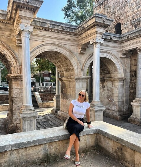 A woman sitting on a stone bench in front of ancient stone arches. 3