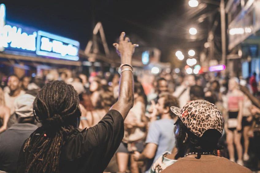 A crowded street at night with people raising their hands, likely at a concert or event. 1