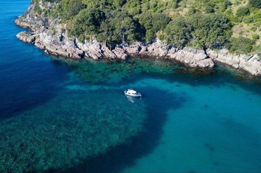 A boat in clear turquoise waters near a rocky coastline with dense greenery. 2
