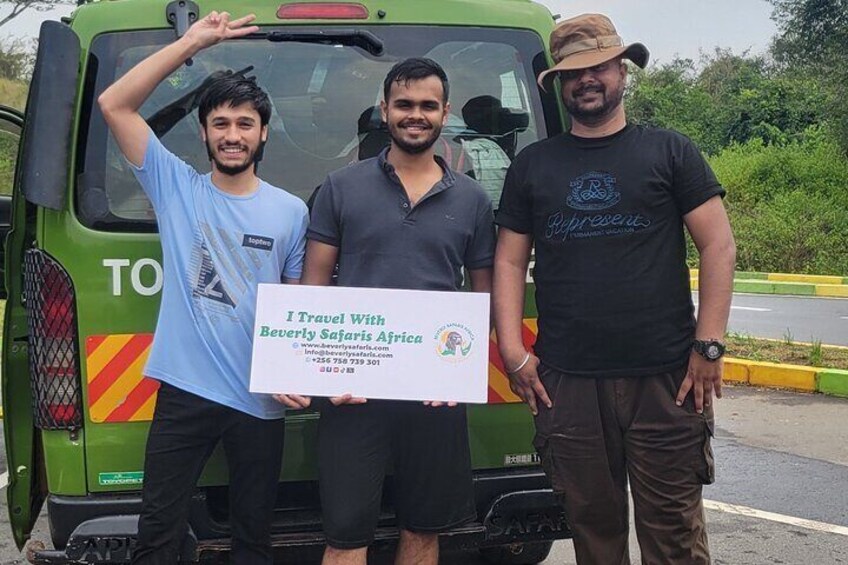 Trois personnes se tiennent devant un véhicule de safari vert et tiennent une pancarte sur laquelle on peut lire : « Je voyage avec Beverly Safari Africa ». 3