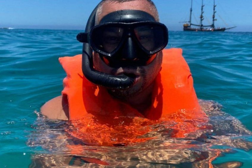 Una persona practica snorkel en aguas azul turquesa, con un chaleco salvavidas naranja y un barco al fondo. 4