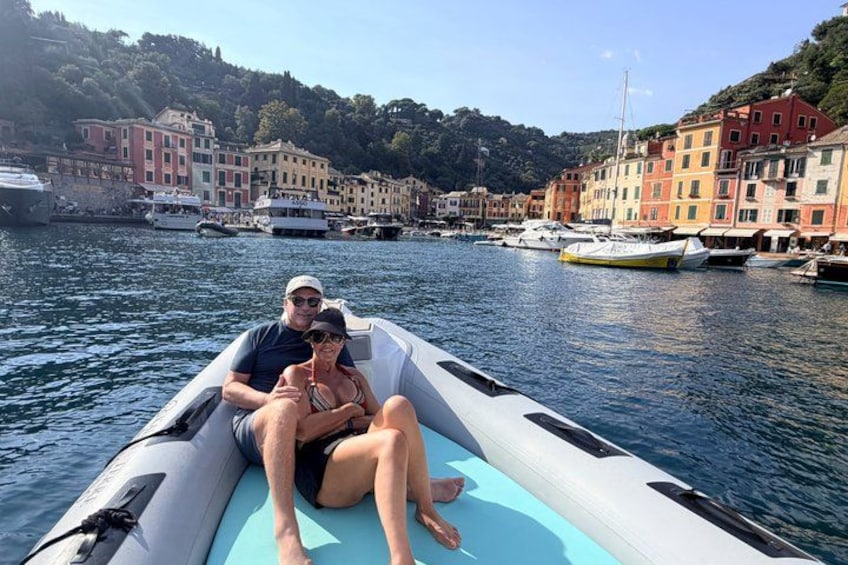 Et par sejler i en motorbåd i en havn med farverige bygninger i baggrunden. 1