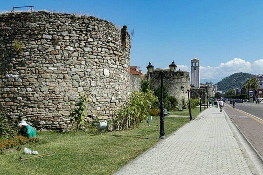 Un mur de pierre, un chemin pavé et une rue bordée d’immeubles et surmontée d’un beffroi. 3
