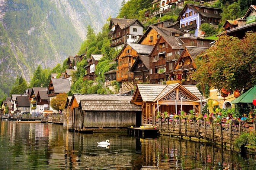 A lakeside village with wooden houses, a wooden boathouse, and a white swan on the water. 1