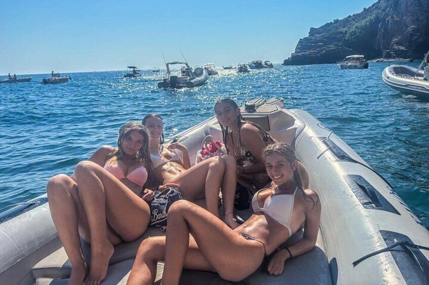 Un grupo de personas en un bote, en el agua, con otros botes y acantilados al fondo. 3