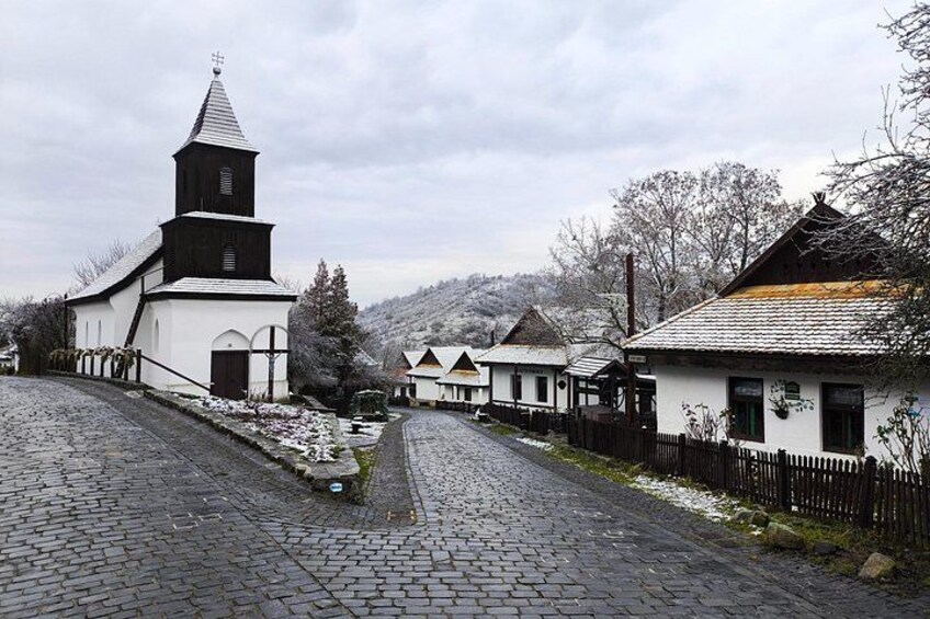 A cobblestone street lined with traditional buildings, including a church with a steeple and a white facade. 3