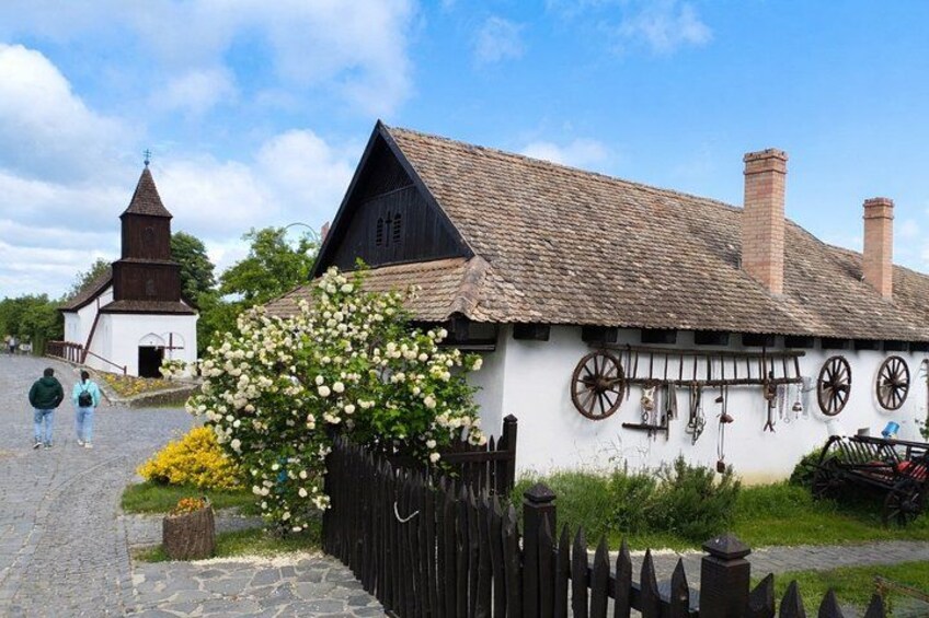 A traditional European village with a church, a white house with wooden wheels, and a wooden fence. 1