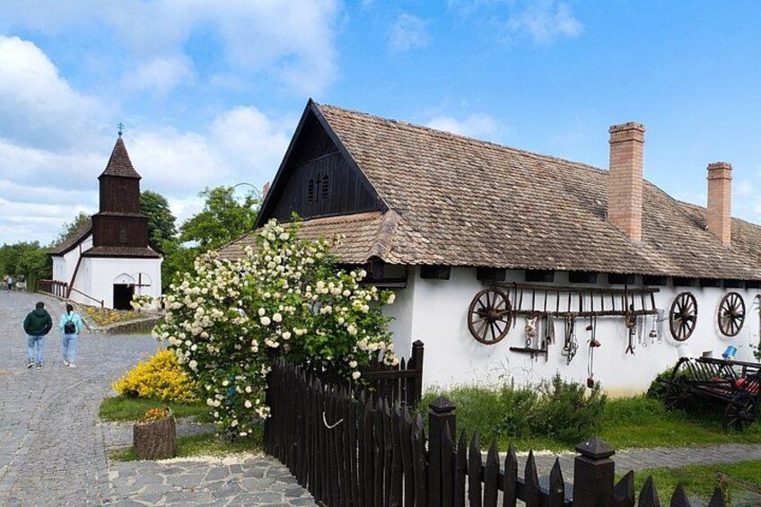 A traditional building with a thatched roof, a wooden fence, and a church in the background. 1