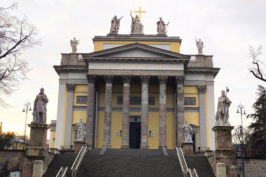 Un edificio amarillo con columnas y estatuas, que presenta una cruz en la parte superior. 2