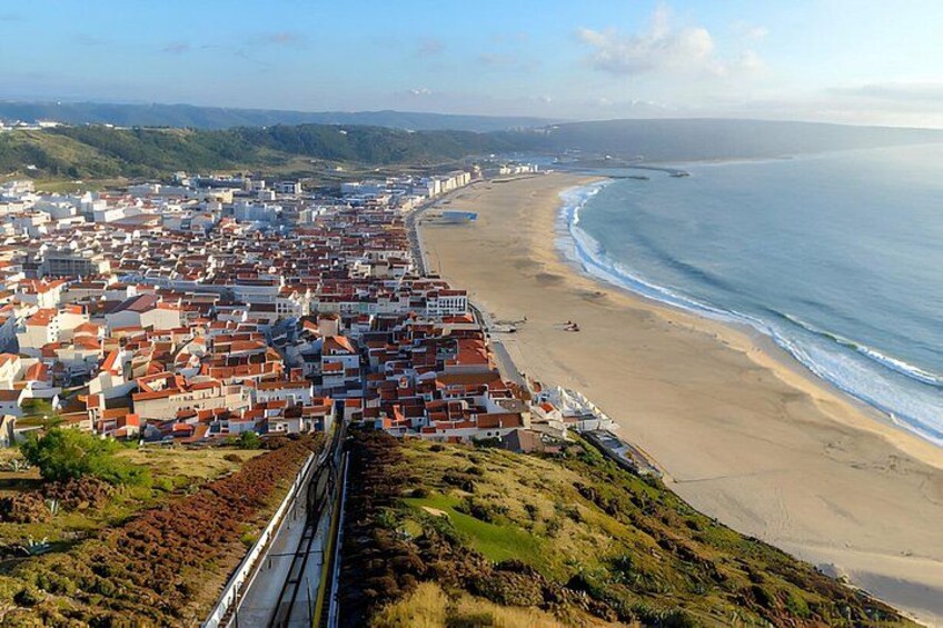 A coastal town with red-roofed buildings, a beach, and a train track. 3