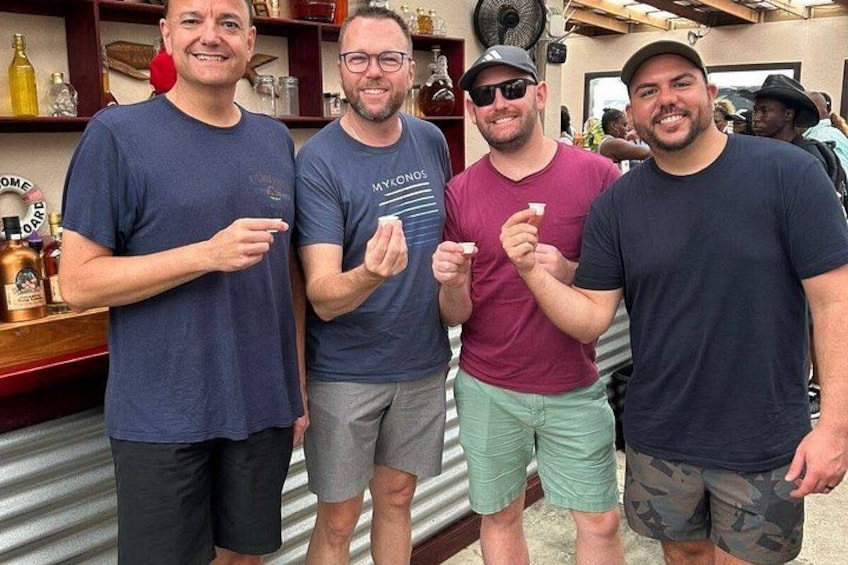 Vier mannen staan binnen, sommigen met drankjes, met in de achtergrond planken vol flessen en glazen. 3