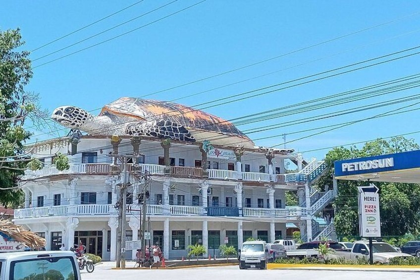 A multi-story building with a distinctive turtle sculpture on the roof, a gas station with a sign, and a clear blue sky. 4
