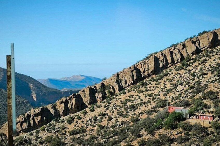 A rocky hillside with sparse vegetation, a small building, and a utility pole. 4
