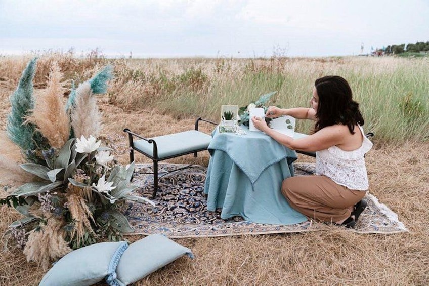 A person arranging a table with a blue cloth and decorative items in a grassy outdoor setting. 3