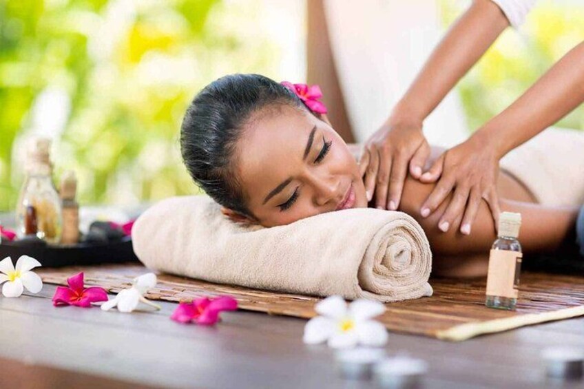 Une personne reçoit un massage sur une table en bois, agrémenté de fleurs et d’huiles essentielles. 1