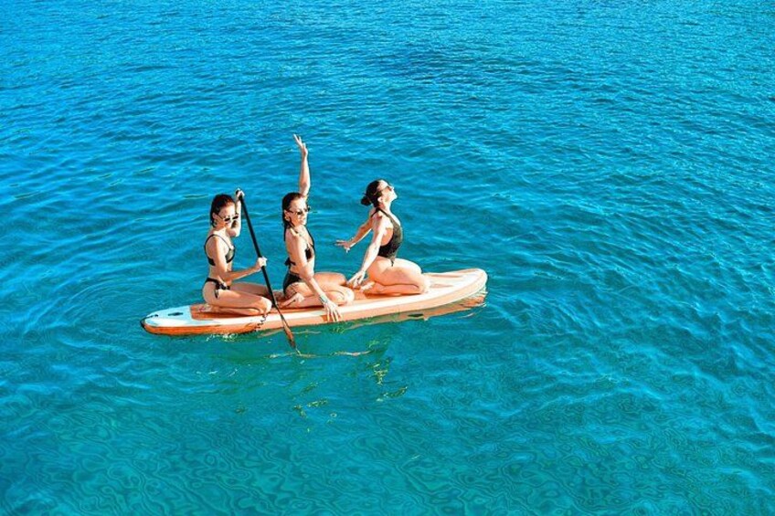 Tres personas en una tabla de remo sobre aguas azules y transparentes. 1