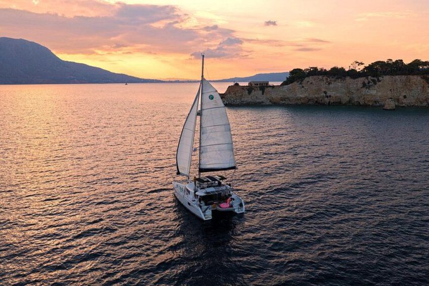 A sailboat on calm waters during sunset with a rocky coastline in the background. 1
