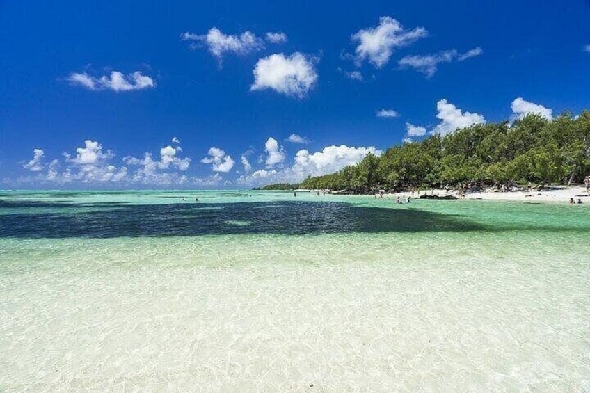 A beach with clear turquoise water, a sandy shore, and a forested hill in the background. 4