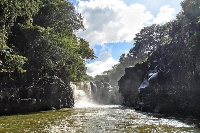 A waterfall cascading down a rocky cliff surrounded by dense greenery. 2