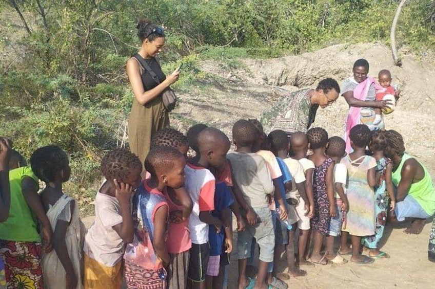 A group of children and adults gathered outdoors, some holding objects, in a natural setting with trees and rocks. 4