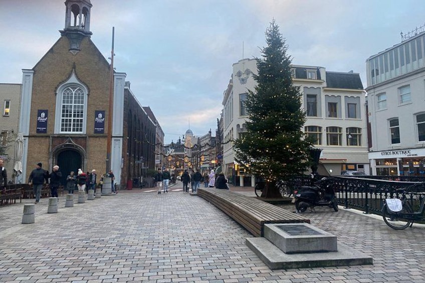 Una plaza empedrada con un árbol de Navidad, una iglesia y edificios con tiendas. 1