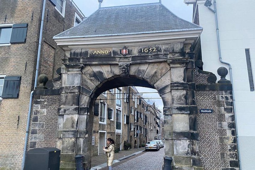 Un arco de piedra con la inscripción 'CANO 1632' y una vista de la calle con edificios y un automóvil estacionado. 2