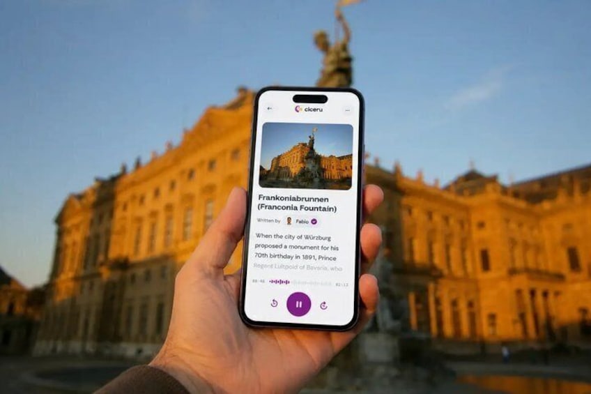 Une main tenant un smartphone affichant des informations sur la fontaine de Frankonia, située dans une ville historique européenne. 1