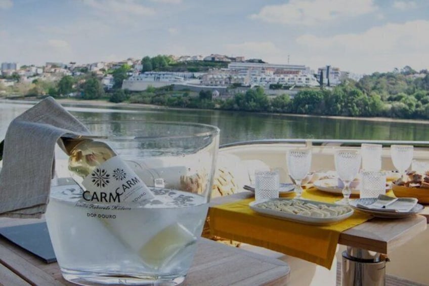 Un tavolo con un bicchiere d'acqua, una bottiglia e un piatto di cibo, con vista su un fiume e degli edifici. 2