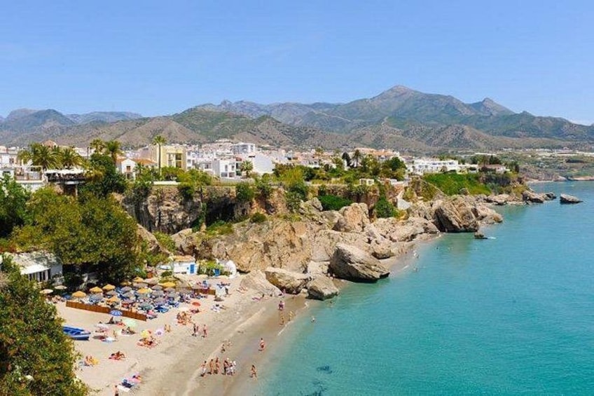 A coastal town with a beach, rocky cliffs, and mountains in the background. 2
