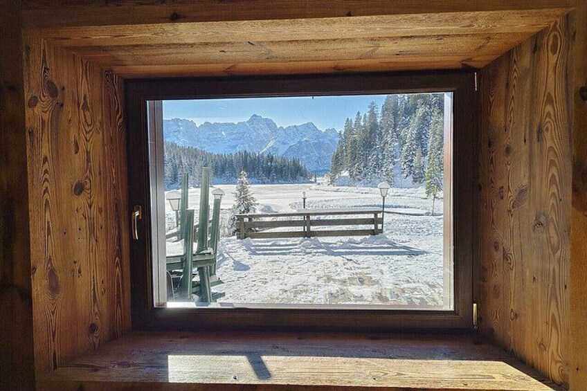 A wooden cabin with a large window overlooking a snowy landscape with mountains and trees. 3
