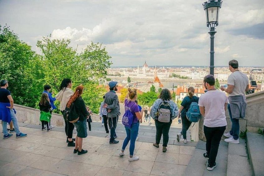 Un grupo de personas se encuentra sobre una escalera de piedra, con vista a un paisaje urbano que destaca una estructura en forma de cúpula. 4