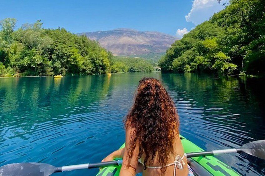 A person kayaking on a calm river surrounded by lush greenery and hills. 1