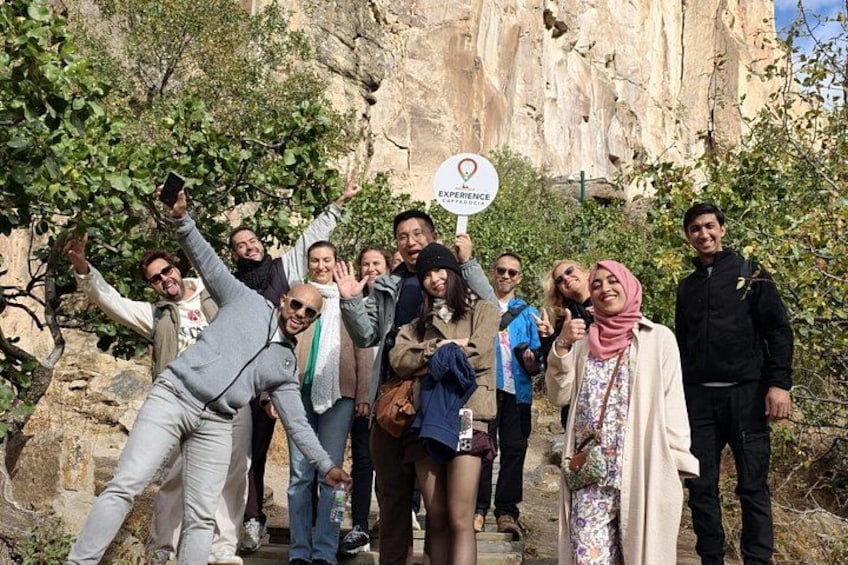 A group of people posing in front of a rocky cliff with a sign that reads 'Experience Cappadocia.' 1