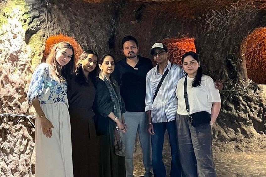 A group of people standing in a cave with rocky walls and orange mineral deposits. 4