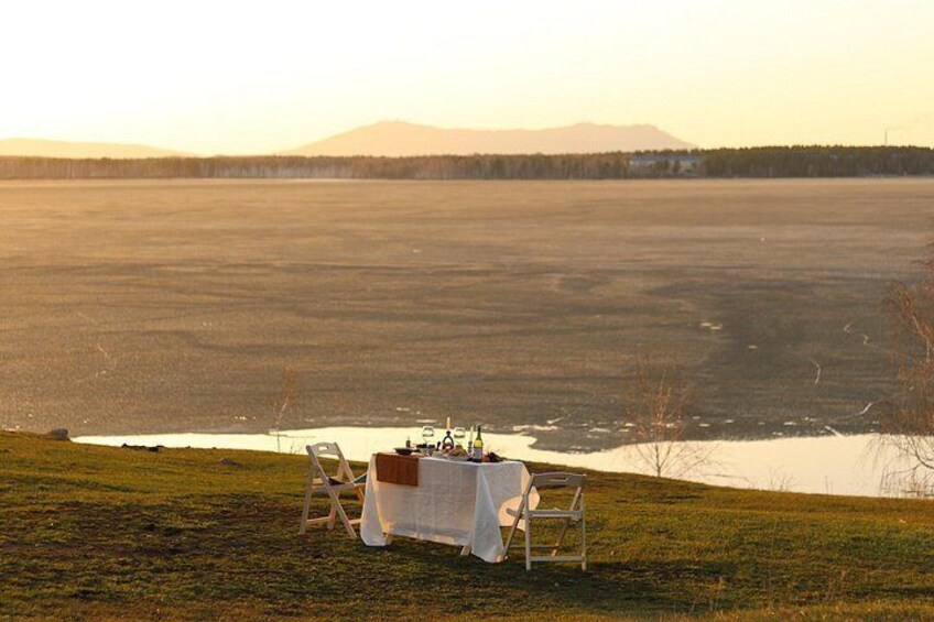 A table set up on a grassy hill overlooking a frozen lake with mountains in the background. 1