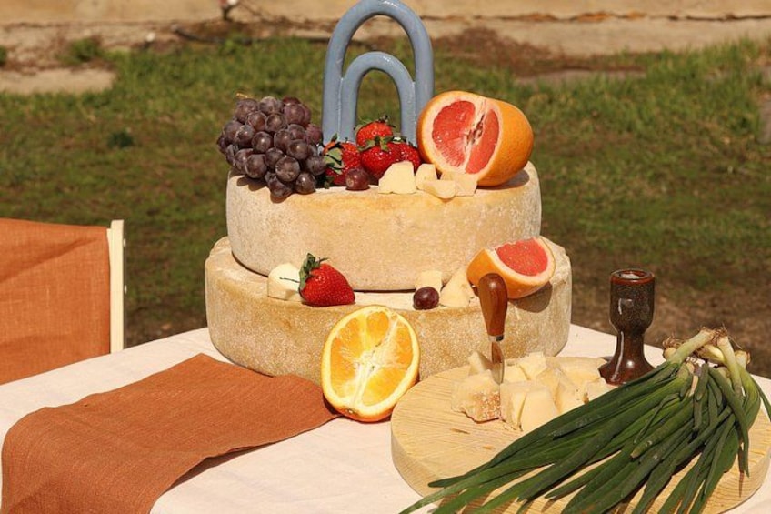 A cheese wheel with grapes, strawberries, and citrus fruits, a knife, a wooden board with herbs, and a rustic setting. 2