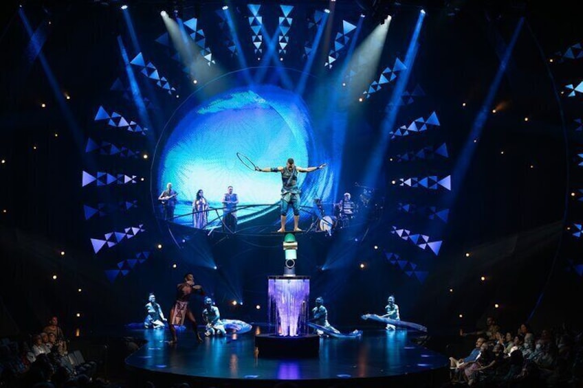 A stage performance with a large screen displaying a blue ocean scene, performers on stage, and a spotlight. 3