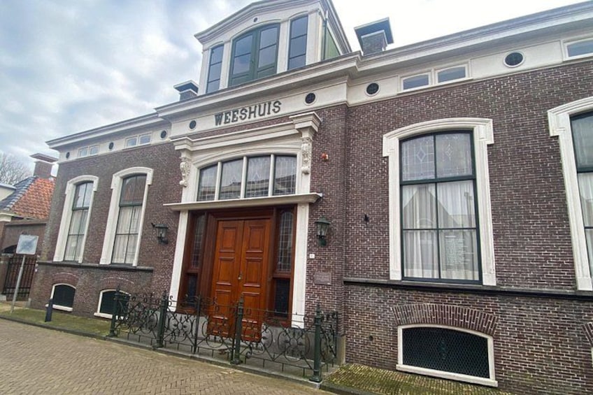 A brick building with a large wooden door and the name 'WEESHUIS' above it. 4