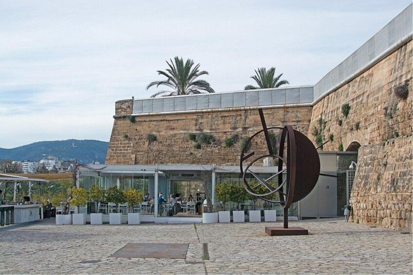 Un cortile con un edificio moderno, una grande scultura in metallo e un muro in pietra. 3