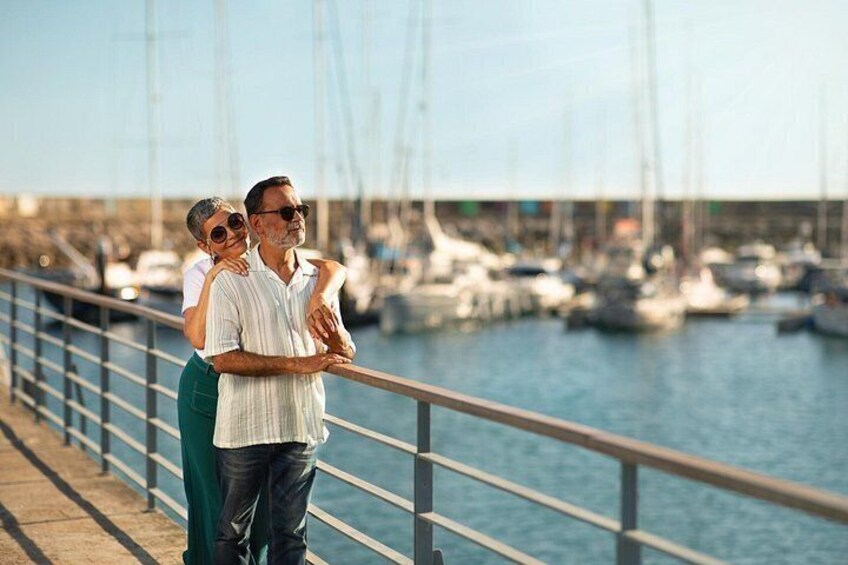 A couple standing on a waterfront promenade with boats in the background. 5