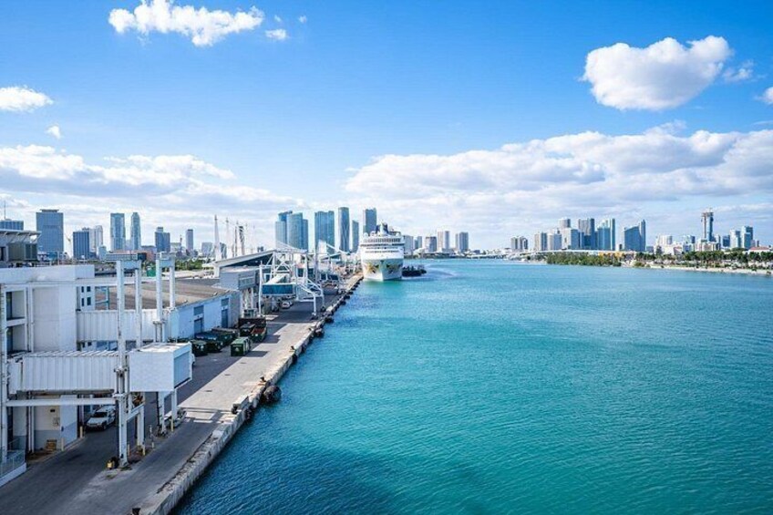 A waterfront cityscape with a cruise ship docked, a marina, and a clear blue sky. 4