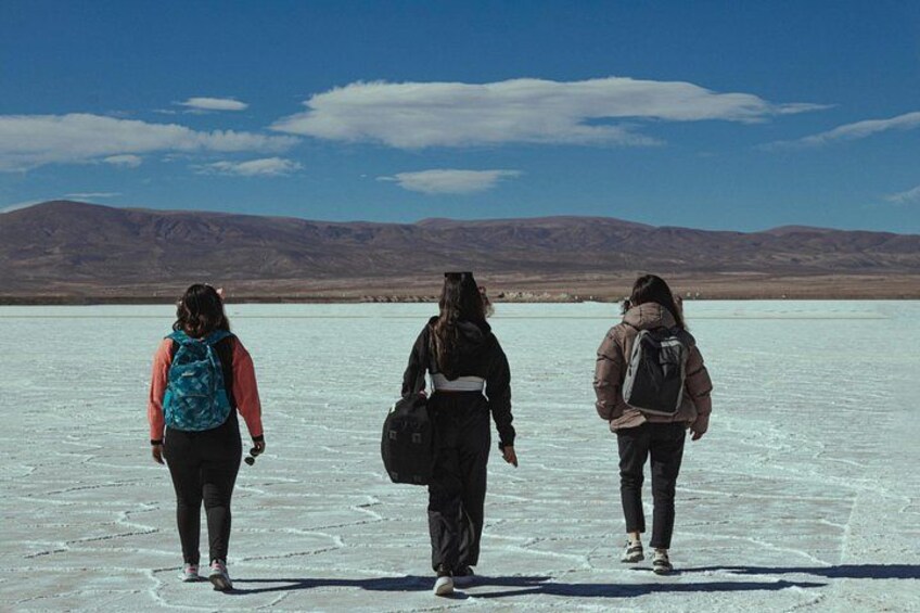 Three people walking on a frozen lake with mountains in the background. 3