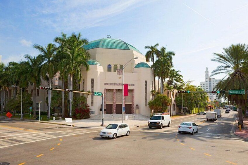 A mosque with a green dome, palm trees, and a street with cars and traffic lights. 4